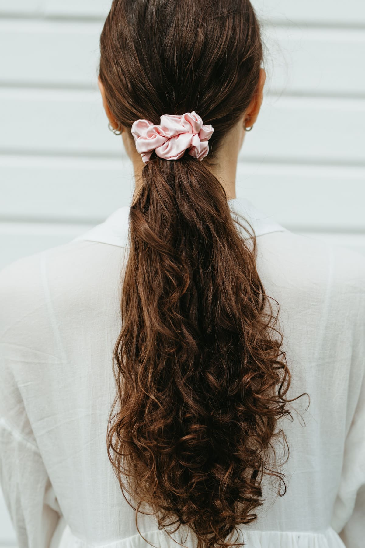 Stor rosa sidensnodd i scrunchie modell i långt brunt lockigt hår