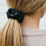 Stor svart sidensnodd scrunchie i ett blont hår. Bild tagen snett bakifrån