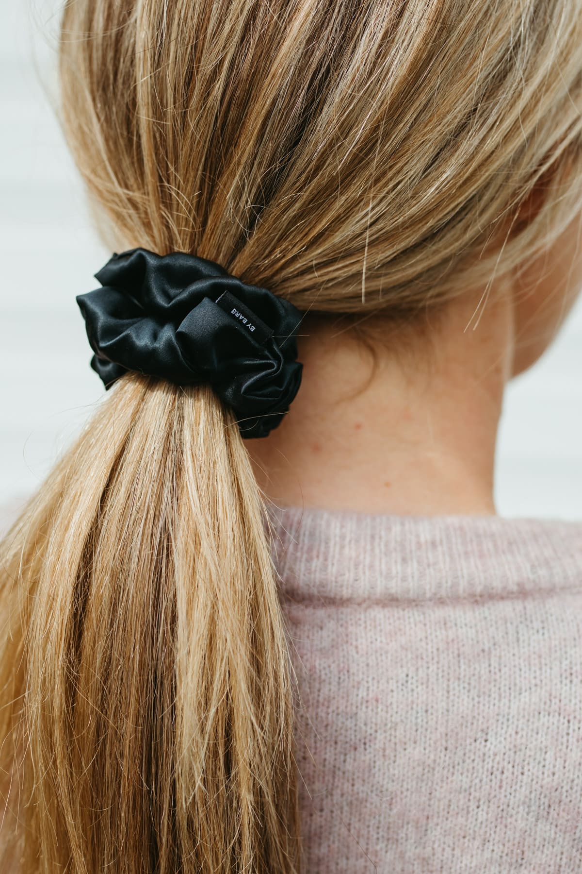 Stor svart sidensnodd scrunchie i ett blont hår. Bild tagen snett bakifrån