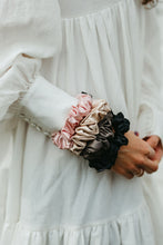 Ladda upp bild till gallerivisning, Stora sidensnoddar scrunchies i beige, svart, rosa, mörkgrå på en handled på kvinna med vit klänning
